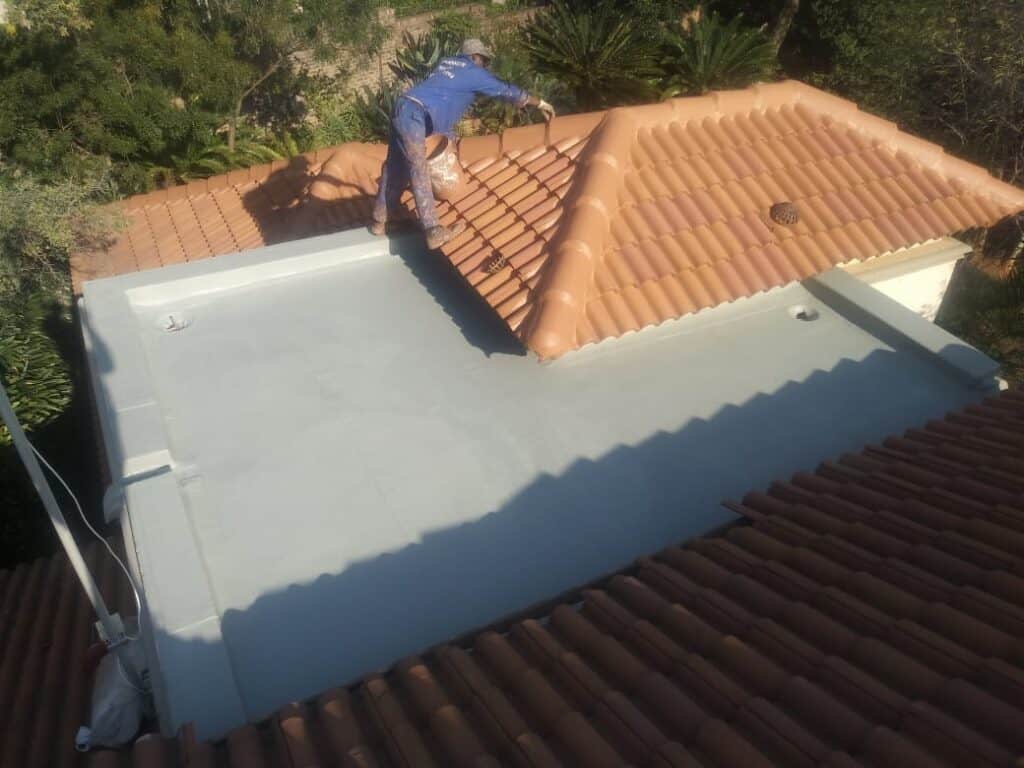 Worker applying waterproofing to concrete roof surface with terracotta tiles.