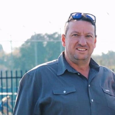 Man in work shirt with sunglasses on head, outdoors, smiling.