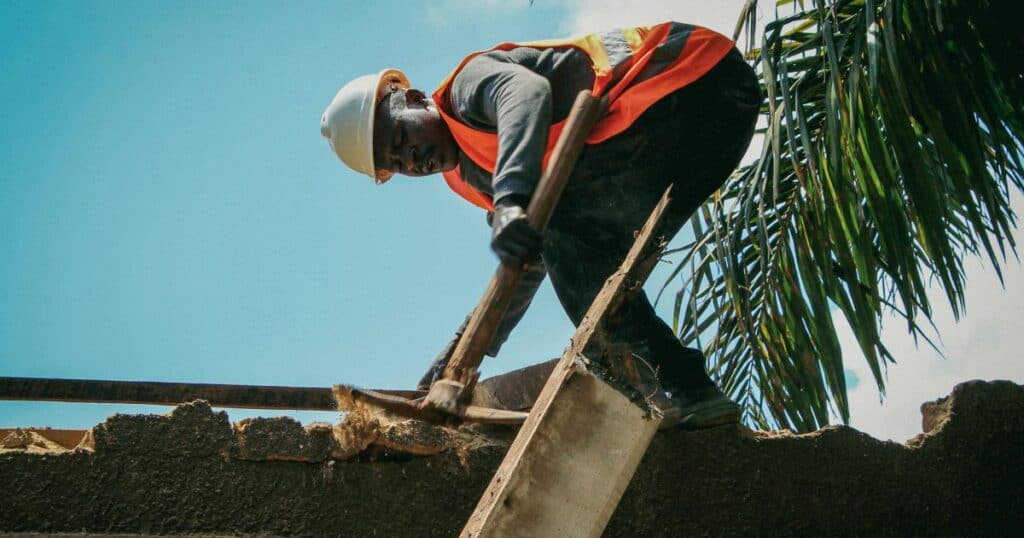 Roofing worker in safety gear installing roof tiles on a building.