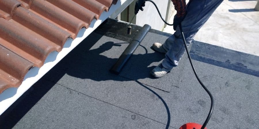 Worker inspecting and repairing a roof with a roller tool.