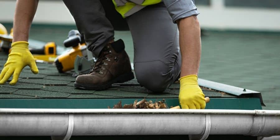 Roof repair worker inspecting shingles on a residential roof.