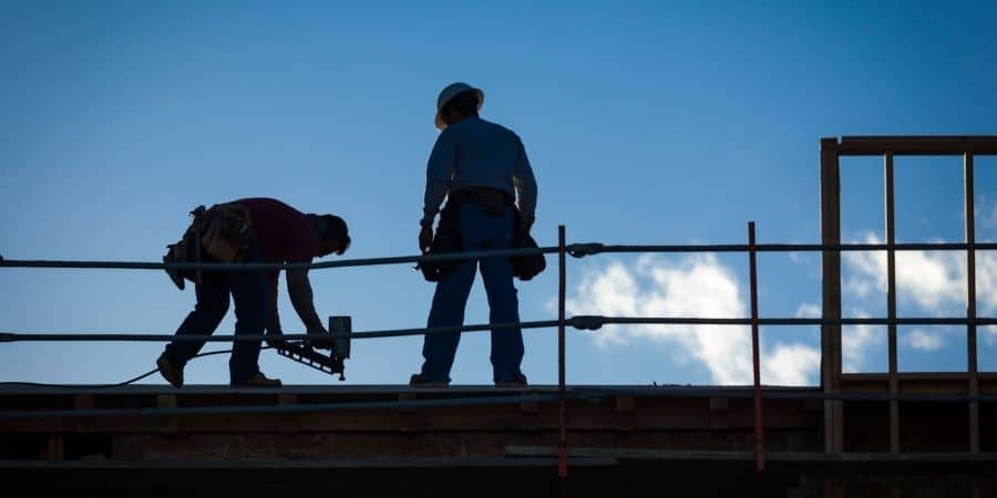 Construction workers installing roofing on a building under construction.