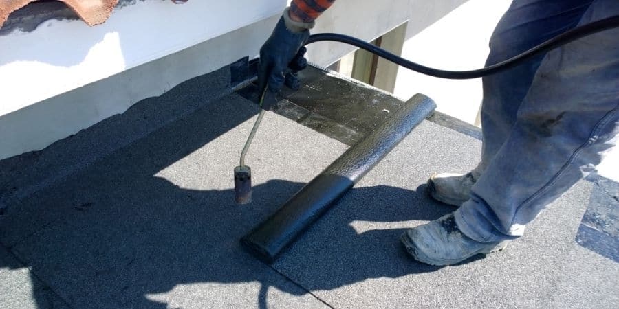Worker applying waterproofing membrane on office building roof.