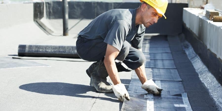 Worker applying waterproofing membrane on office building roof.
